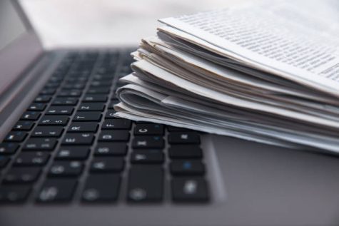 Pile of daily papers with news on the computer